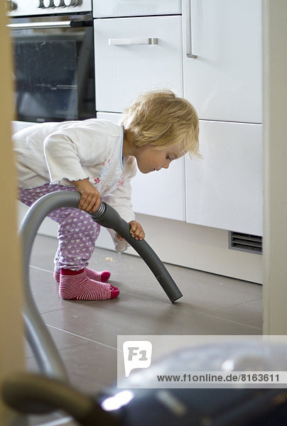 Girl cleaning kitchen with hoover