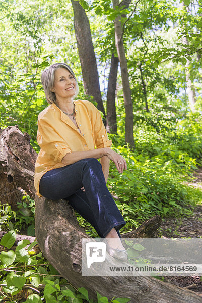 Senior woman sitting on log in forest