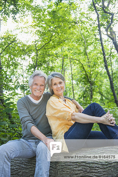 Senior couple sitting on log in forest