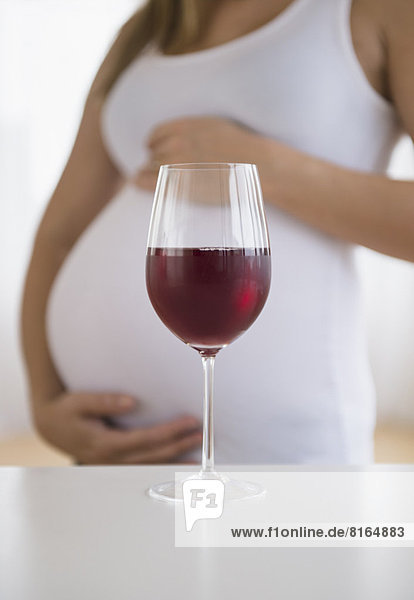 Mid section of pregnant woman  red wine in front