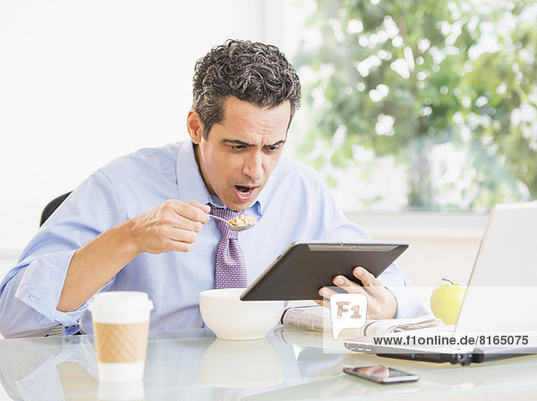Portrait of man eating and using digital tablet