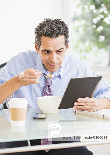 View of mature man eating cereal and using digital tablet