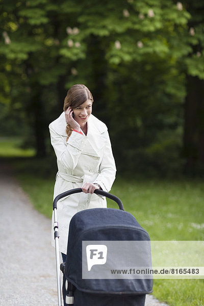 Mother with pram in park talking on mobile phone