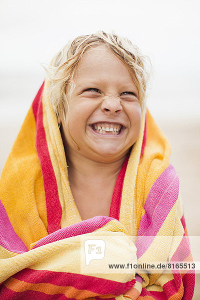 Boy (6-7) wrapped in towel on beach