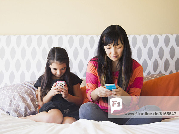 Mother with daughter (8-9) sitting and using cell phones