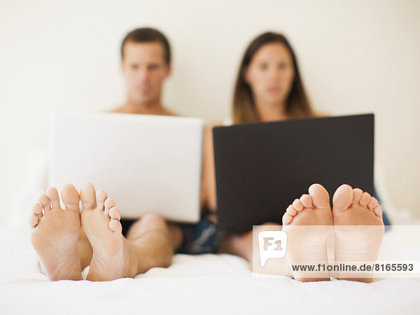 Couple lying on bed with laptops