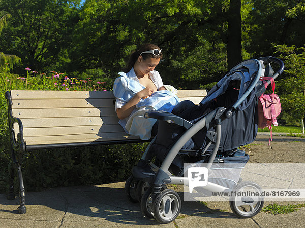 Eine junge Mutter sitzt auf einer Bank und stillt ihr Baby