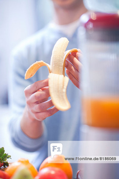 Junger Mann schält Banane für Fruchtgetränk