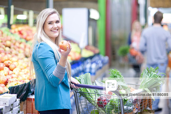 Junge Frau hält Apfel in der Markthalle
