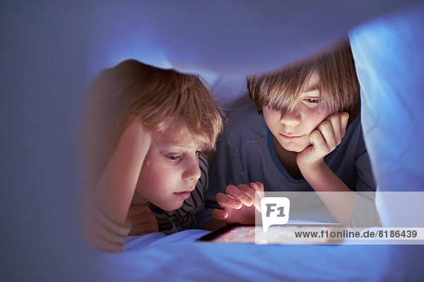 Brüder unter der Bettdecke mit digitalem Tablett