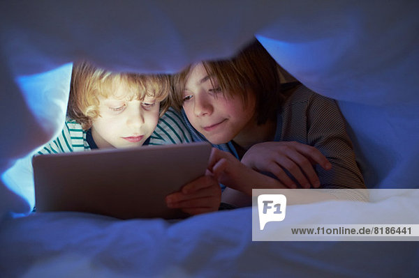 Brüder unter der Bettdecke mit digitalem Tablett