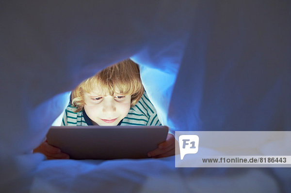 Junge unter der Bettdecke mit digitalem Tablett