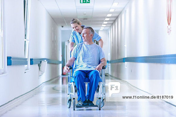 Krankenschwester schiebt Patient im Rollstuhl den Flur hinunter
