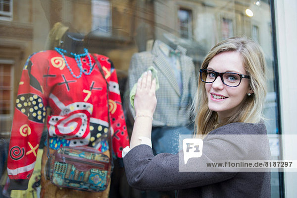 Woman cleaning window of clothes shop