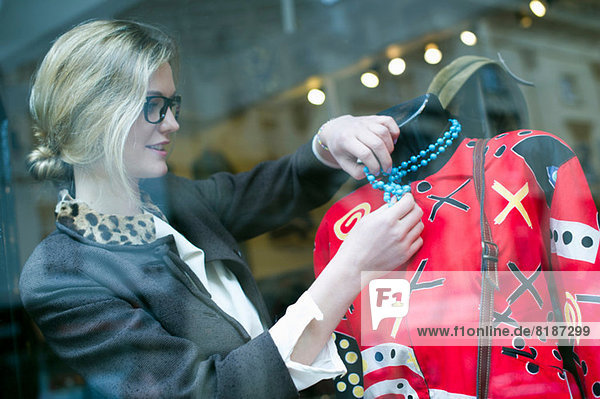 Woman putting necklace on shop dummy