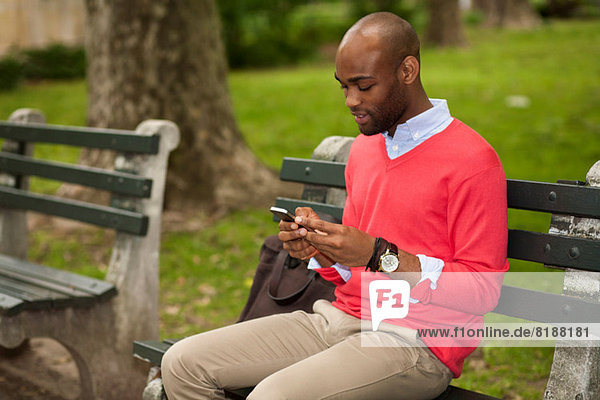 Junger Mann sitzt auf der Parkbank mit dem Handy