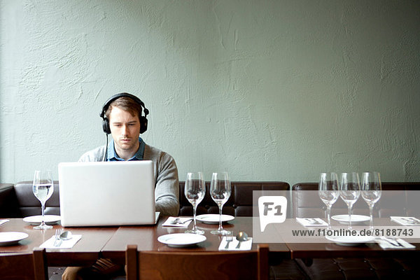 Junger Mann mit Kopfhörer und Laptop im Restaurant