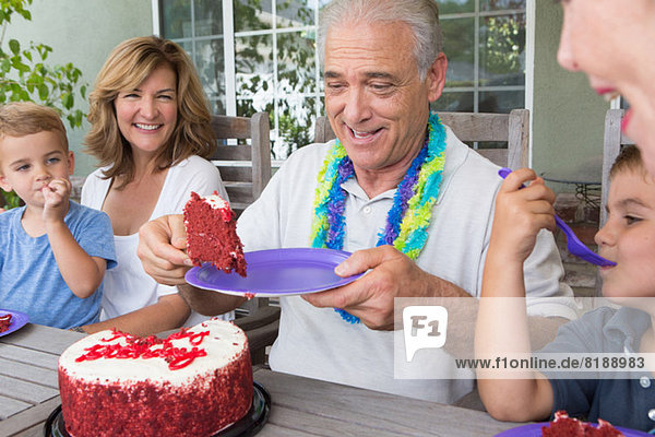 Senior Mann serviert ein Stück Geburtstagskuchen auf einer Party mit der Familie.