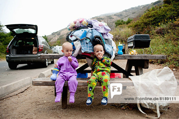 Toddler twins eating banana on picnic bench