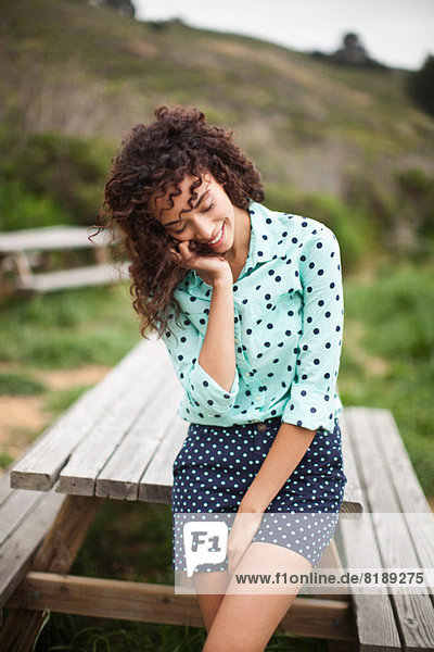 Junge Frau mit Hand im Haar am Picknicktisch stehend  lächelnd
