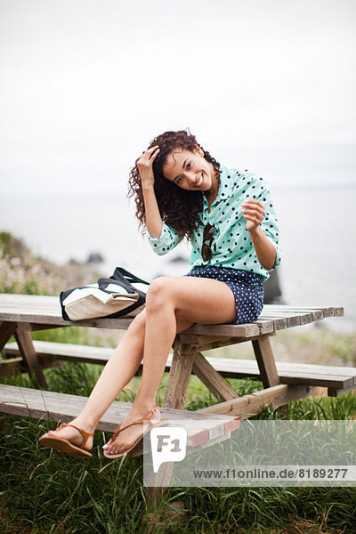 Young woman sitting on picnic table smiling  portrait