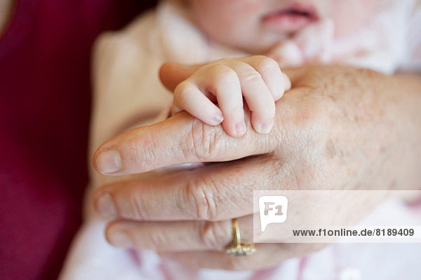 Baby girl holding senior woman's hand  close up