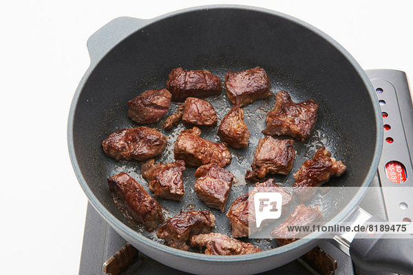 Still life of meat frying in pan on hob