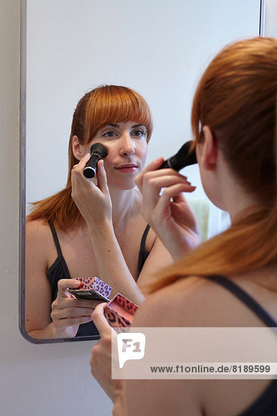 Mid adult woman applying blusher in mirror