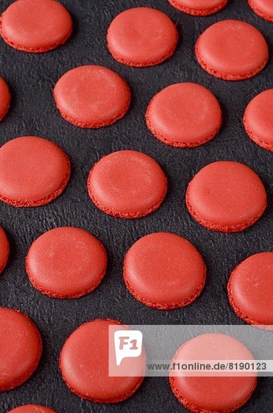 Frisch gebackene rote Macaron-Hälften auf Schiefer-Hintergrund