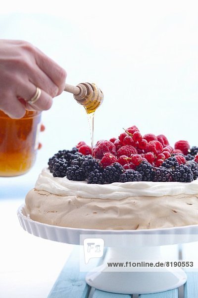 Honig auf Pavlova mit Beeren träufeln