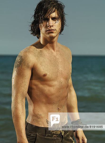 Mann mit nackter Brust und nassen Haaren am Meer