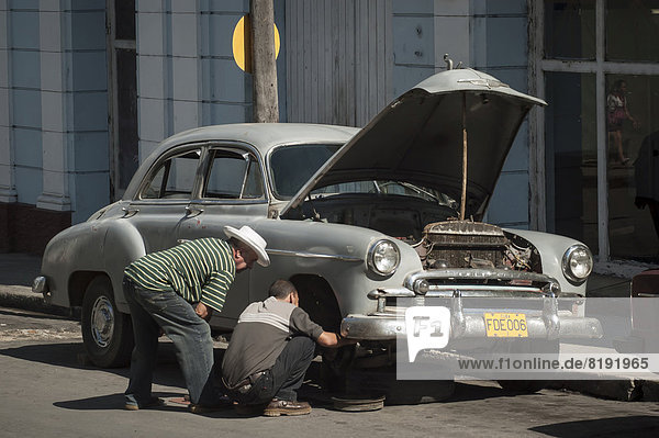 Zwei Männer reparieren einen Oldtimer in einer Straße von Cienfuegos