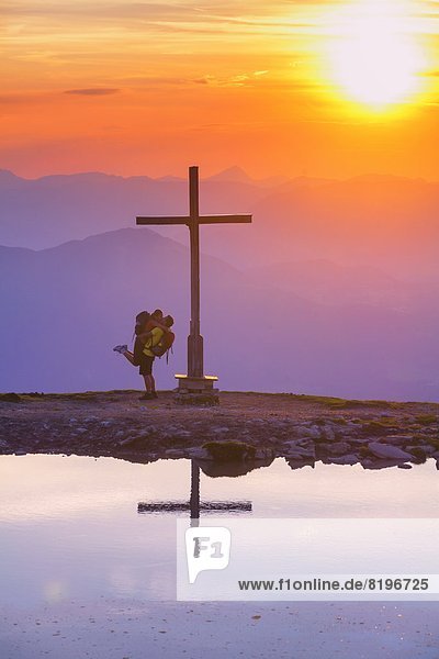 Paar bei Sonnenuntergang beim Gipfelkreuz in der Osterhorngruppe Salzburger Land Österreich