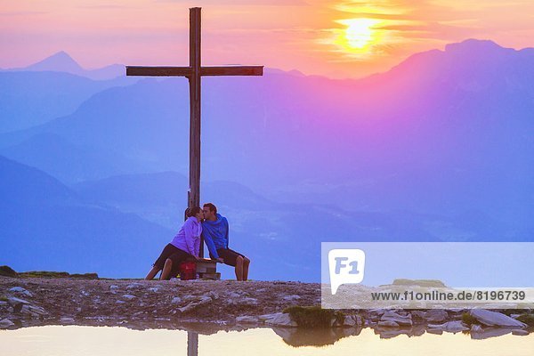Paar küsst sich bei Sonnenuntergang beim Gipfelkreuz in der Osterhorngruppe Salzburger Land Österreich