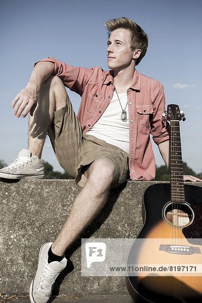 Deutschland  Junger Mann auf der Wand sitzend mit Gitarre