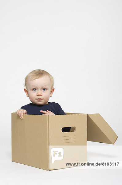 Portrait of baby boy sitting in box on white background