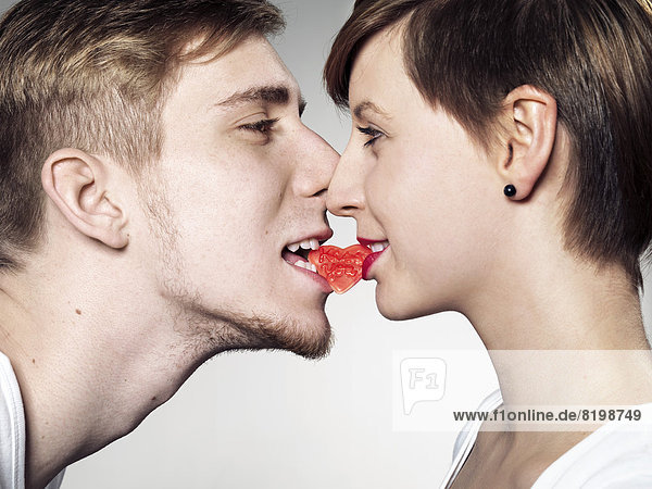 Junger Mann und Frau beißen herzförmigen Süßigkeiten  Mund