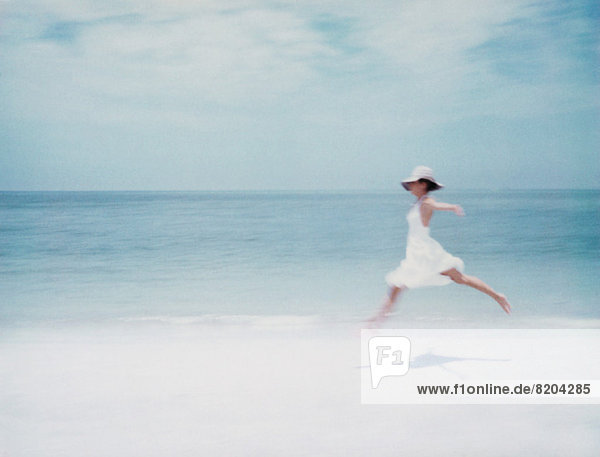 Junge Frau im Kleid springt am Strand  Arme aus  Seitenansicht