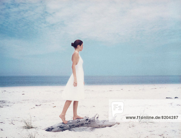 Junge Frau auf Treibholz am Strand stehend  Seitenansicht