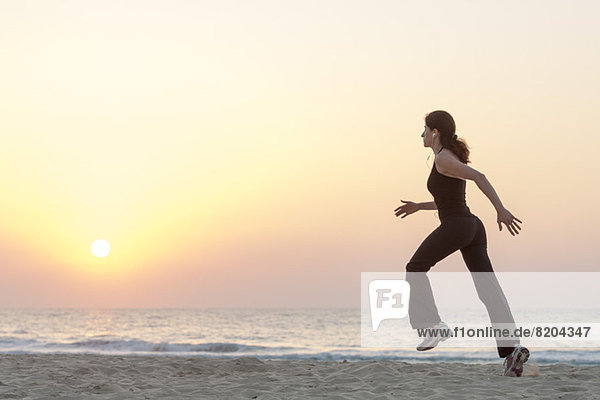 Woman jogging on beach at sunrise with earphones  side view