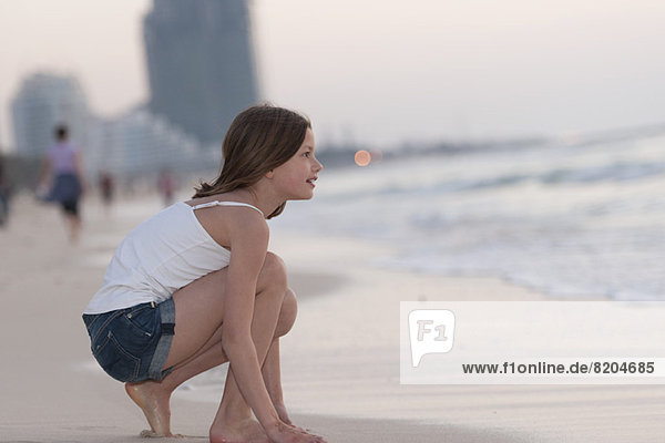 Girl crouching on beach  looking at water