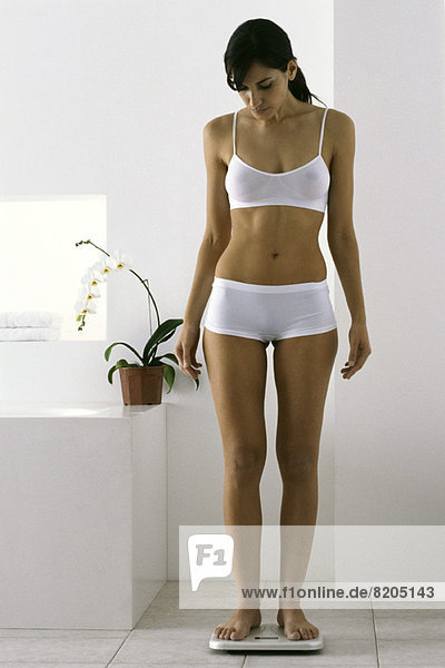 Young woman standing on bathroom scale in underwear