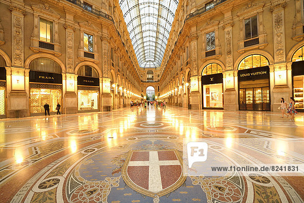 Luxury shopping arcade  roofed gallery of Galleria Vittorio Emanuele II  twilight shot at the blue hour  marble floor mosaic with the coat of arms of Milan