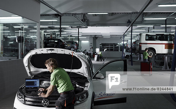 Automechaniker bei der Fehlersuche mit Laptop bei einem PKW in einer Autowerkstatt VW Strasser