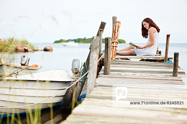 Woman sitting on jetty  reading book