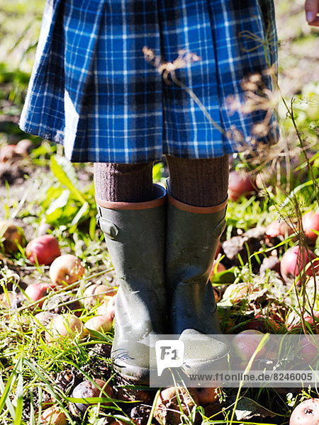 Girl wearing wellingtons standing on fallen apples