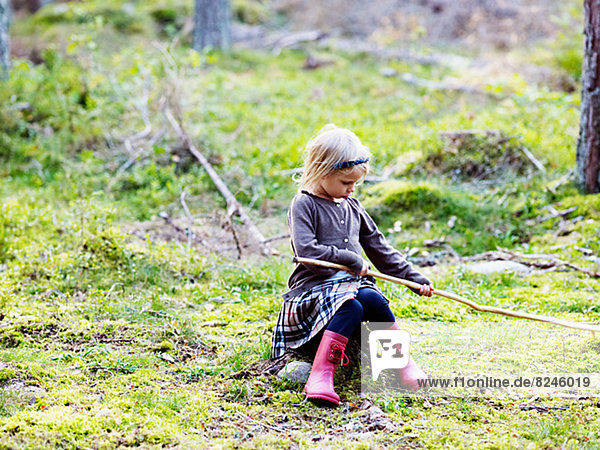 Girl sitting on tree stump and holding stick