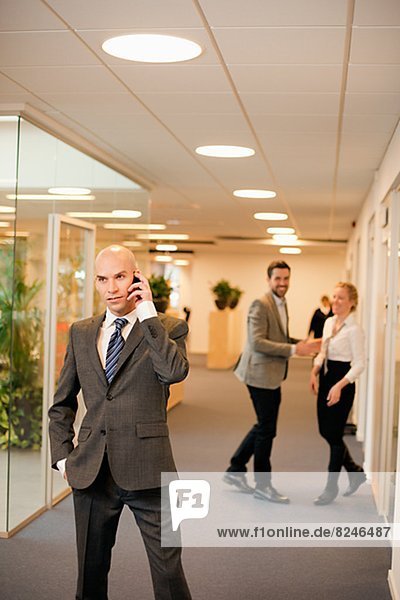 Young businessman on phone in office  smiling colleagues in background
