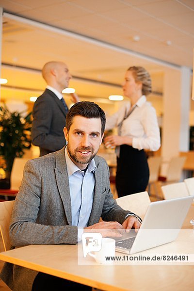Portrait of young businessman in cafeteria with laptop