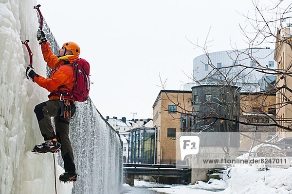 Man ice climbing up frozen waterfall in urban area